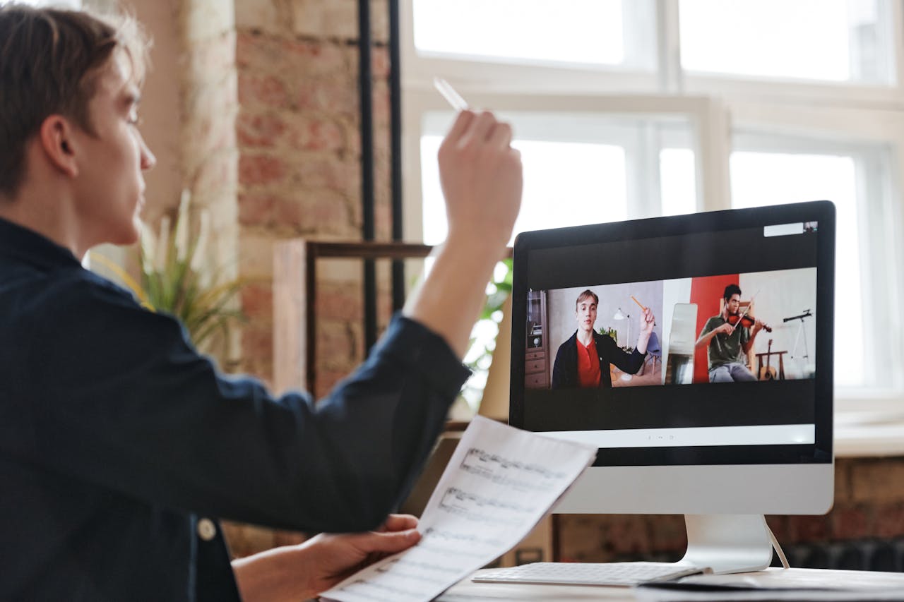 A man participates in a virtual music lesson, interacting with a violin teacher via video call.